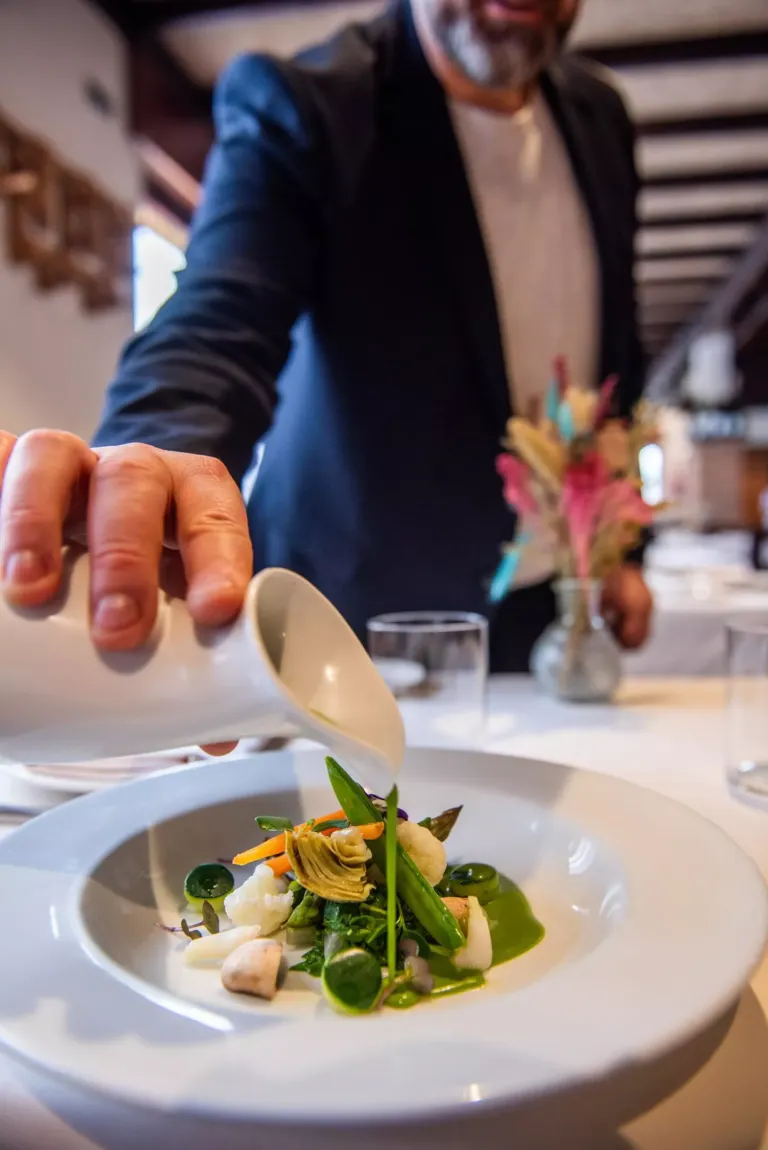 Foto del maitre sirviendo salsa en plato de alcachofas